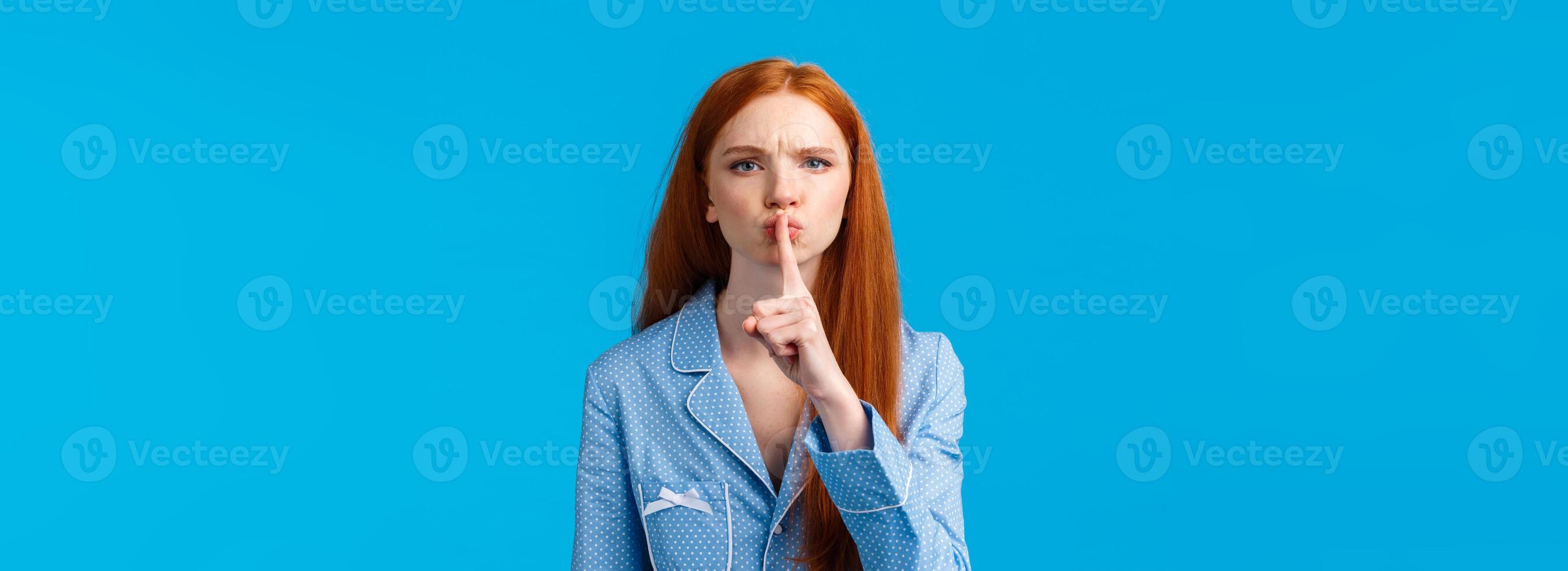 Quiet please Im trying sleep. Displeased and disturbed young redhead college girl living dormitory asking roommate be silent, shushing, say hush angry frowning, press index finger to lips photo