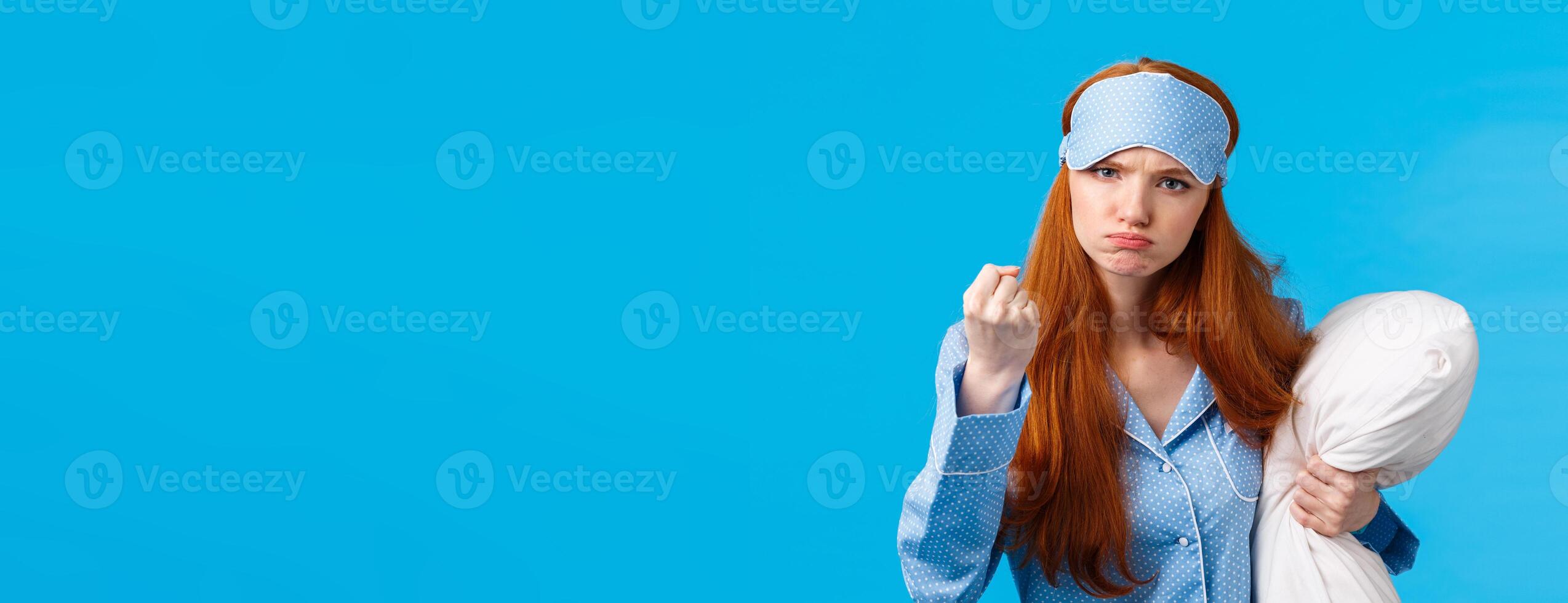Who disturbed my sleep. Mad and displeased, angry grumpy redhead woman threaten sibling being too loud in morning, shaking fist frowning, holding pillow, wearing pyjama and sleep mask photo