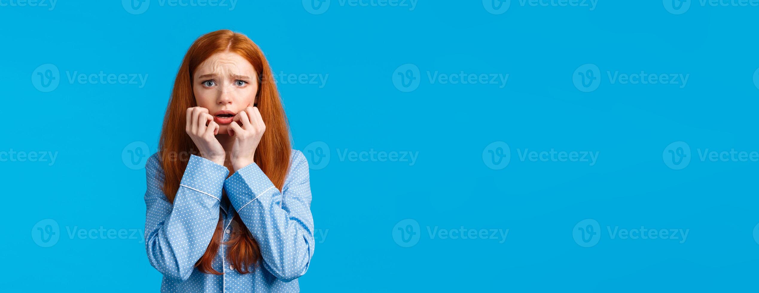 Scared and panicking young worried redhead teenage girl having sleepover with girlfriend, telling scary stories, frowning alarmed, hold hands near mouth as trembling fear, wear nightwear photo