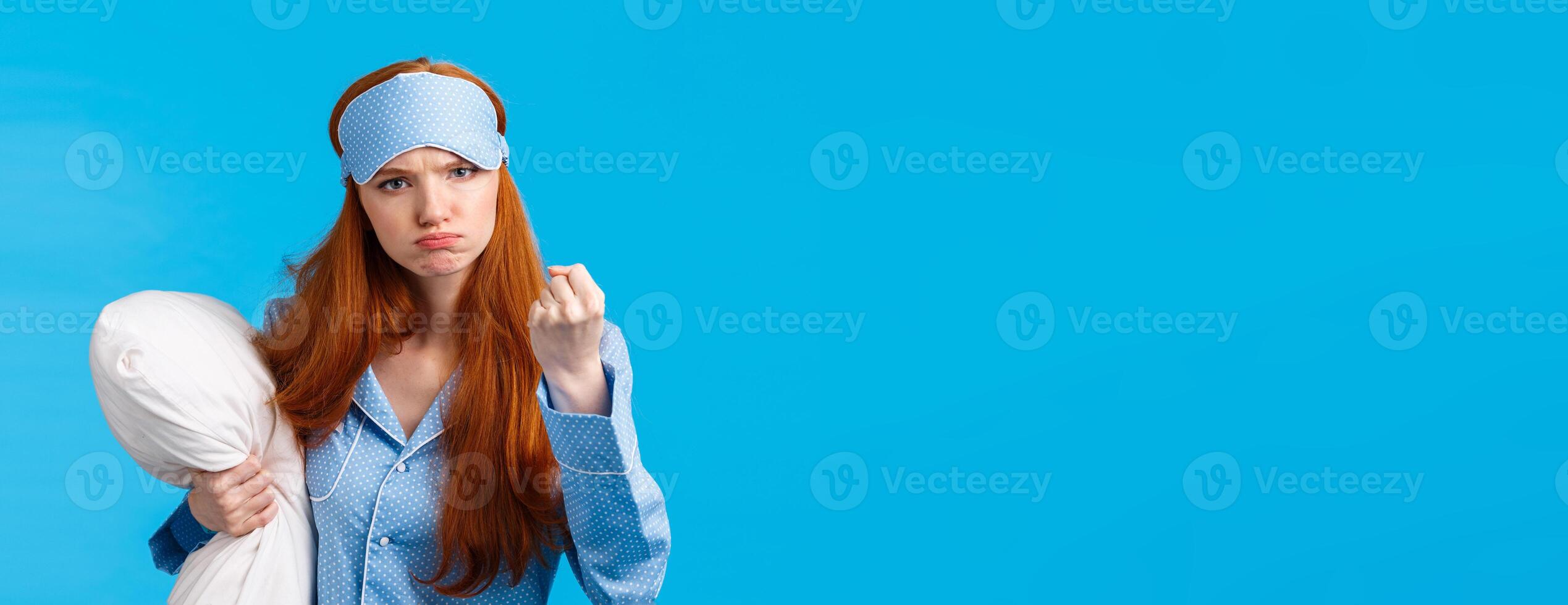 Who disturbed my sleep. Mad and displeased, angry grumpy redhead woman threaten sibling being too loud in morning, shaking fist frowning, holding pillow, wearing pyjama and sleep mask photo