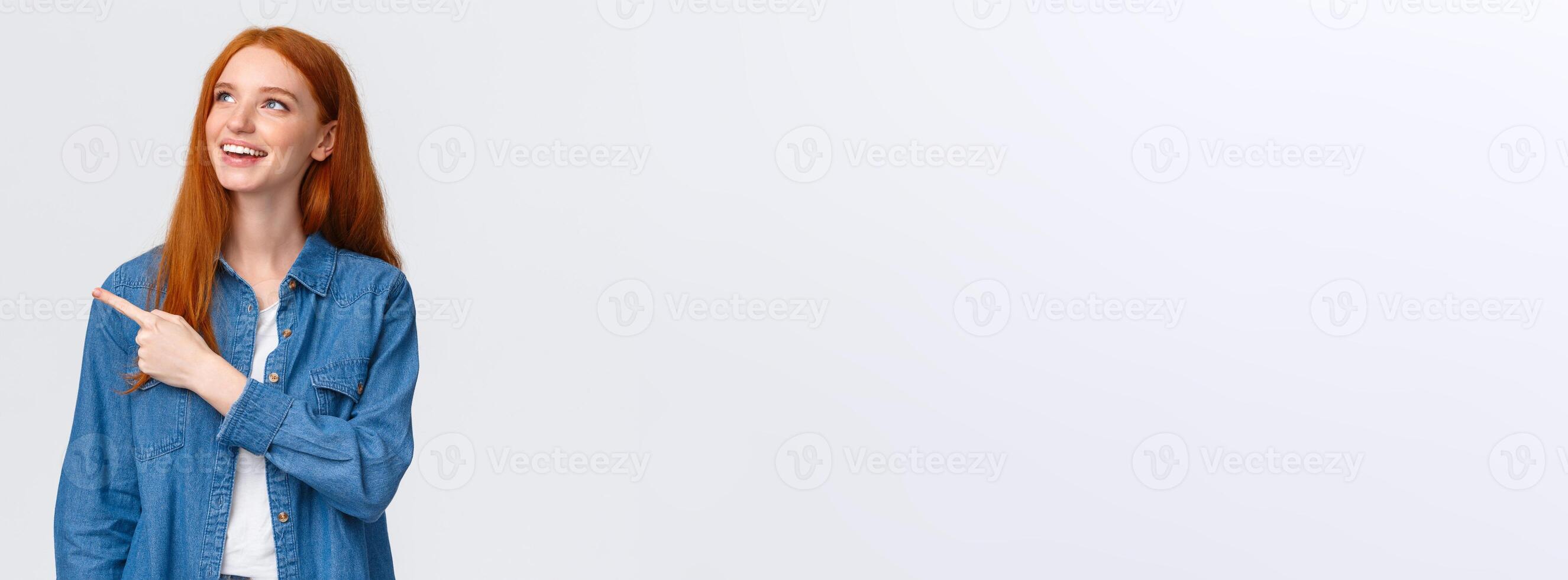 Dreamy carefree good-looking redhead european woman in denim shirt, looking pointing upper left corner, smiling delighted, making choice, seeing perfect product, recommend company service photo