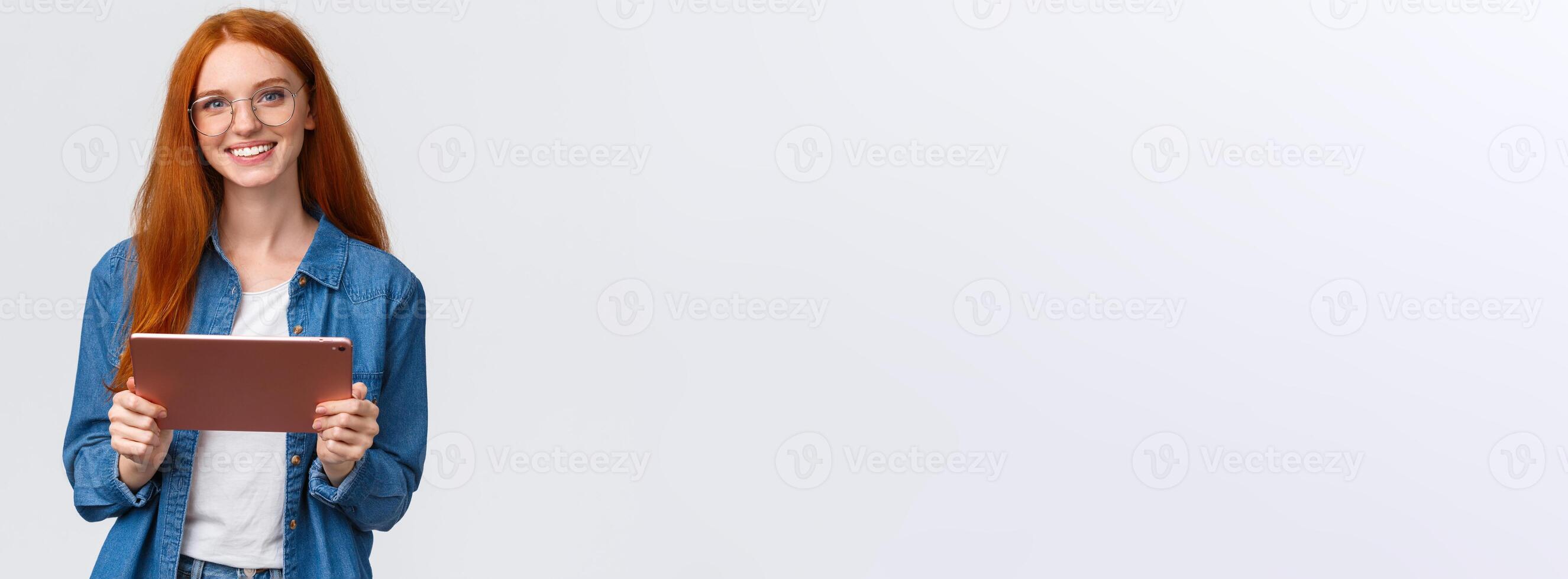 Education, people and teamwork concept. Cheerful pretty redhead millennial female coworker introducing project to team, holding digital tablet, wearing glasses, smiling at camera photo
