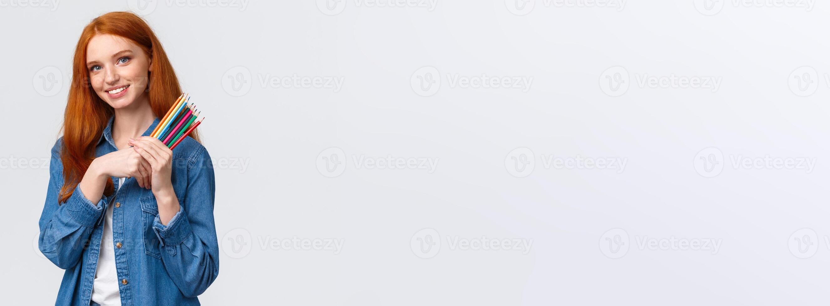 Good-looking charismatic dreamy redhead female in denim shirt, looking camera thoughtful and imaging, want draw something, have design project in mind, holding colored pencils, white background photo