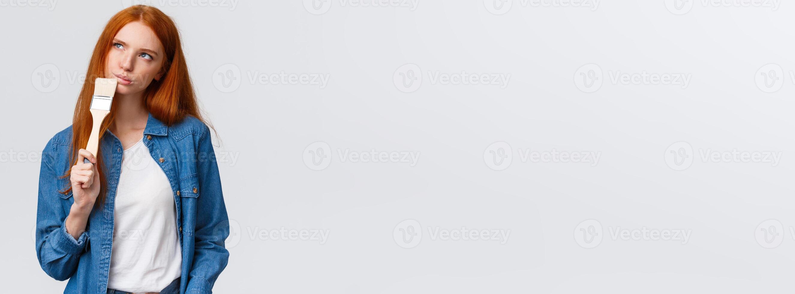 Thoughtful and creative redhead female imaging what colour paint room, holding paintbrush, look up thoughtful, thinking choices, pondering ideas, standing white background unsure photo