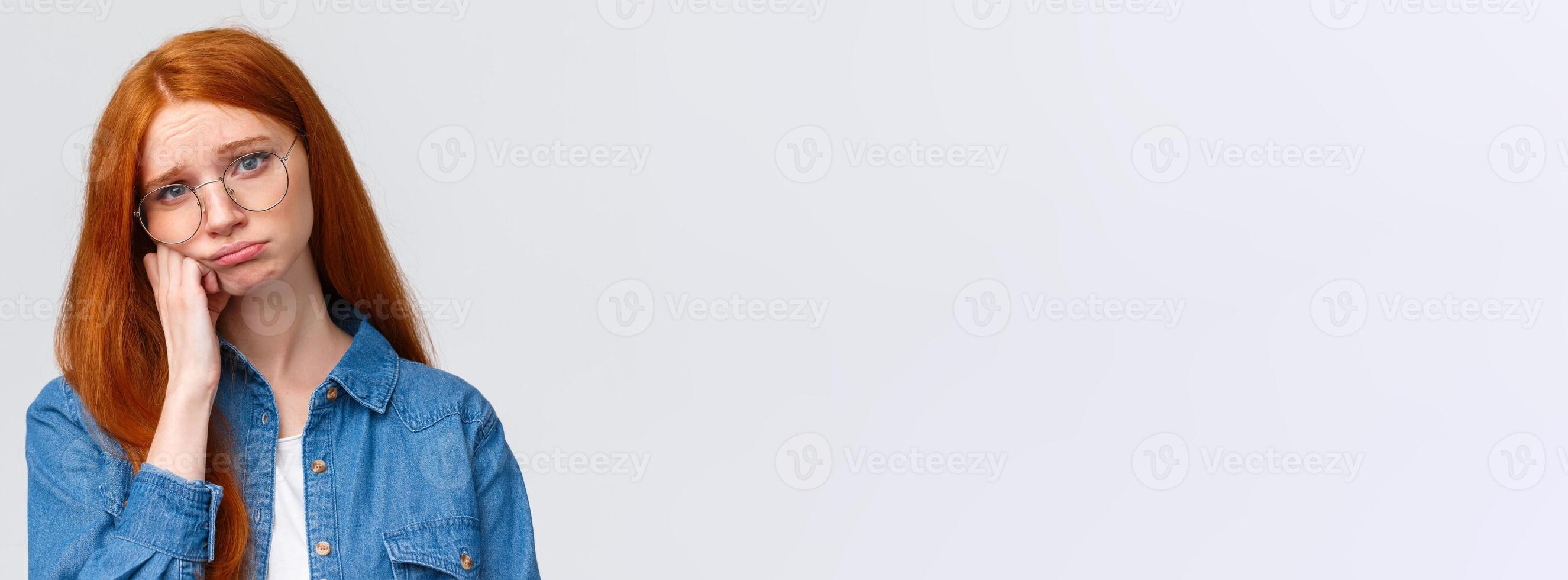 Close-up portrait gloomy unhappy redhead sad girl in glasses, teenager having bad day at college, leaning on hand pouting and sobbing, feeling hurt and distressed, standing depressed white background photo