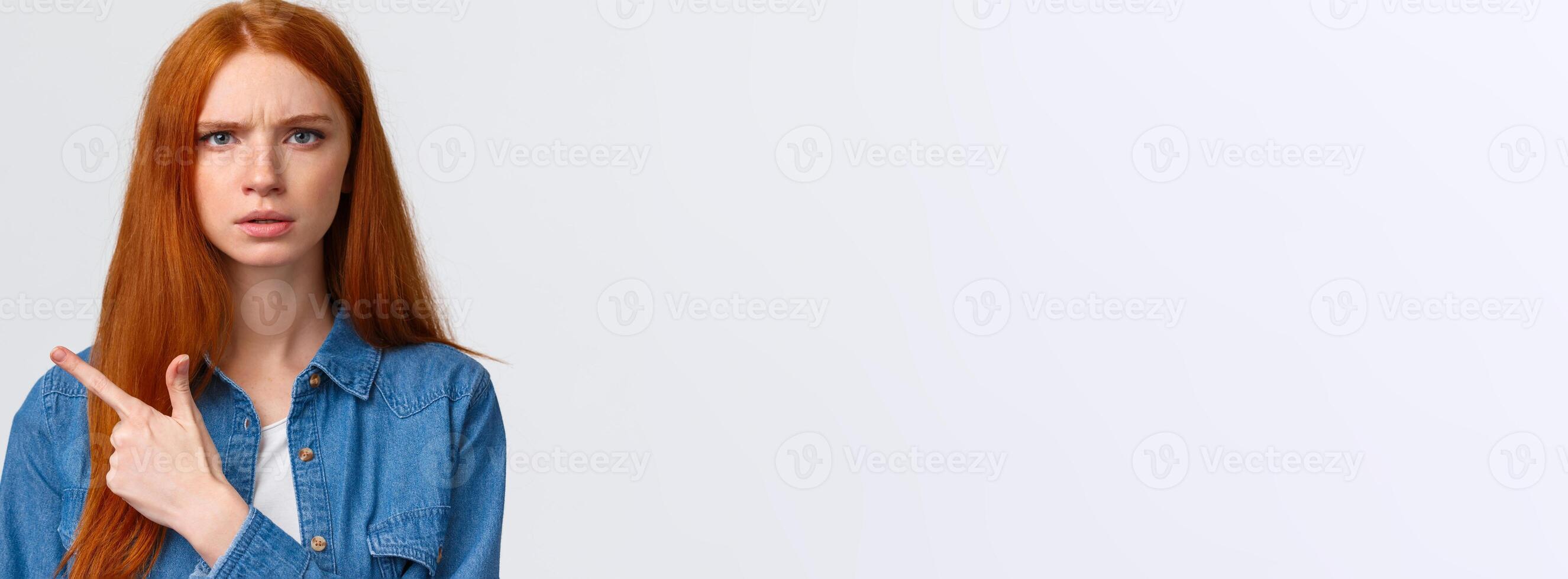 Close-up portrait serious-looking skeptical and displeased angry bothered redhead girlfriend waiting explanation, demand answers as seing something unplesant, pointing finger left photo