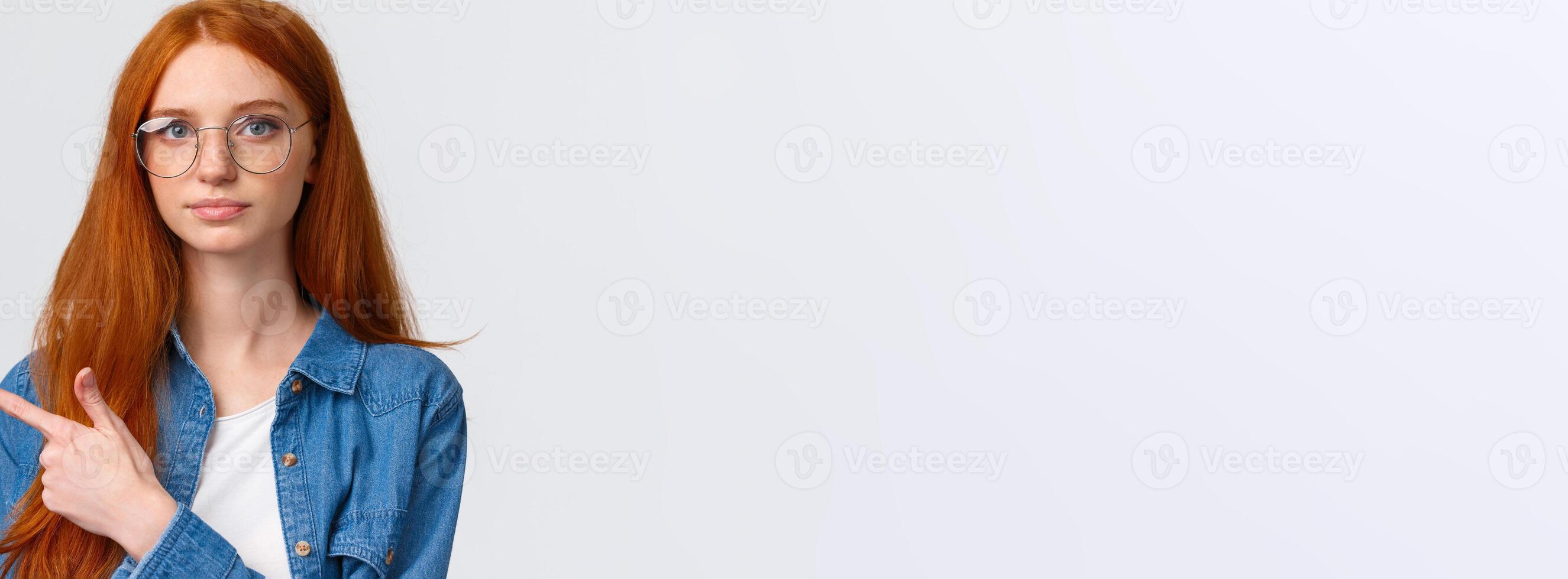 Close-up portrait serious smart and determined young redhead female making strong final choice, pointing finger left and looking camera confident, standing white background photo