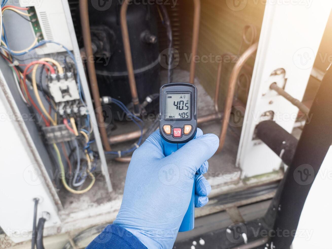 Professional engineer wearing blue gloves using thermo gun for temperature check on the hvac air cinditioning syatem. Temperature check concept on the compressor, condensor , refrigerant system hvac. photo