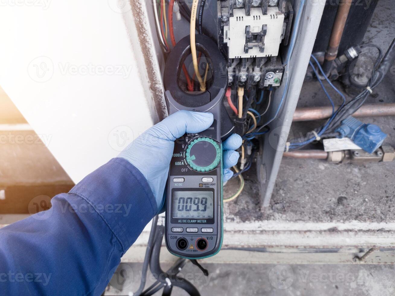 Checking the electric current in the HVAC air conditioning electrical system using an ammeter by an electrician. the enginer wear blue gloves checking electrical system on hvac. photo