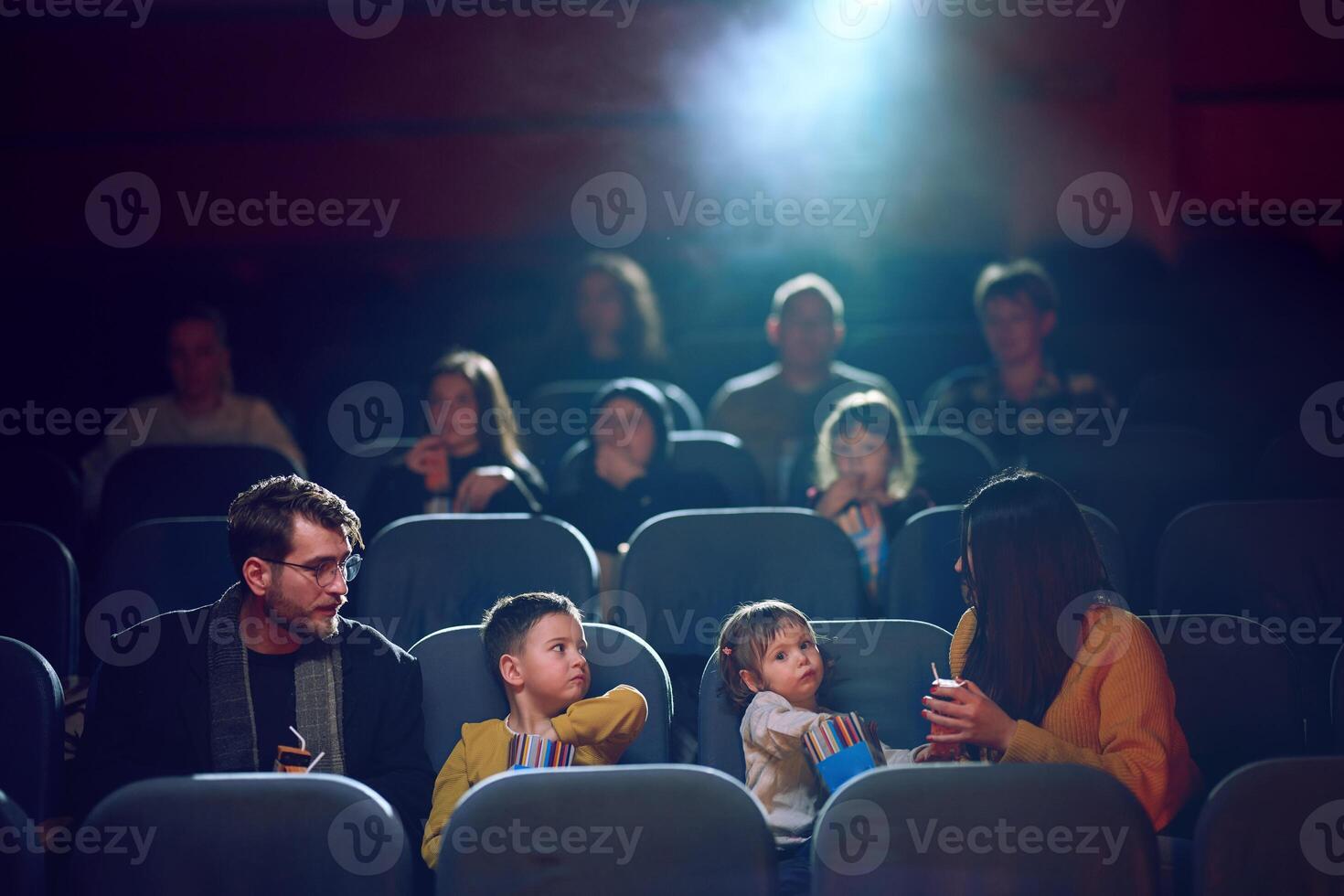 A modern family enjoys quality time together at the cinema, indulging in popcorn while watching a movie with their children photo
