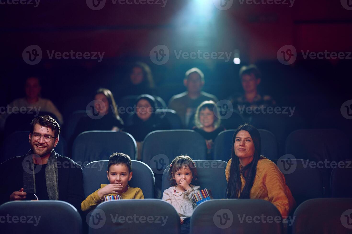 A modern family enjoys quality time together at the cinema, indulging in popcorn while watching a movie with their children photo