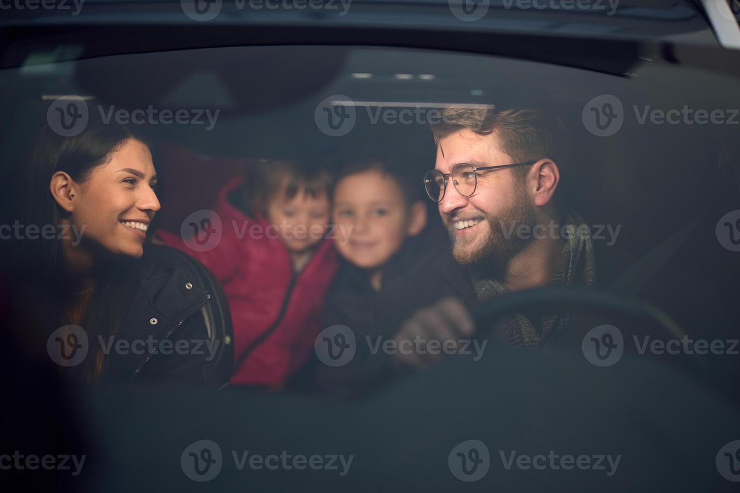 In the nighttime hours, a happy family enjoys playful moments together inside a car as they journey on a nocturnal road trip, illuminated by the glow of headlights and filled with laughter and joy photo