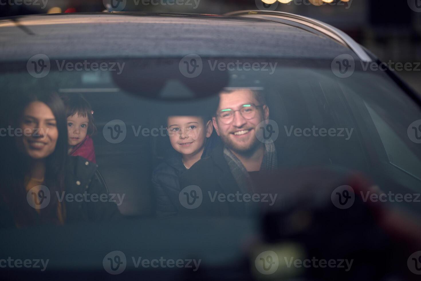 In the nighttime hours, a happy family enjoys playful moments together inside a car as they journey on a nocturnal road trip, illuminated by the glow of headlights and filled with laughter and joy photo