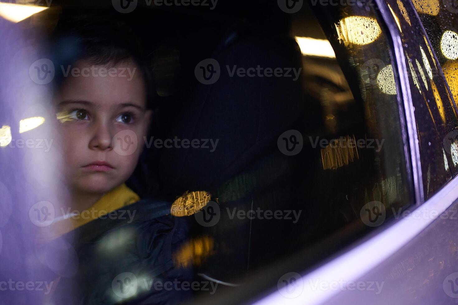 A young boy enjoys a car ride, captured through the window, as he observes the passing scenery. photo