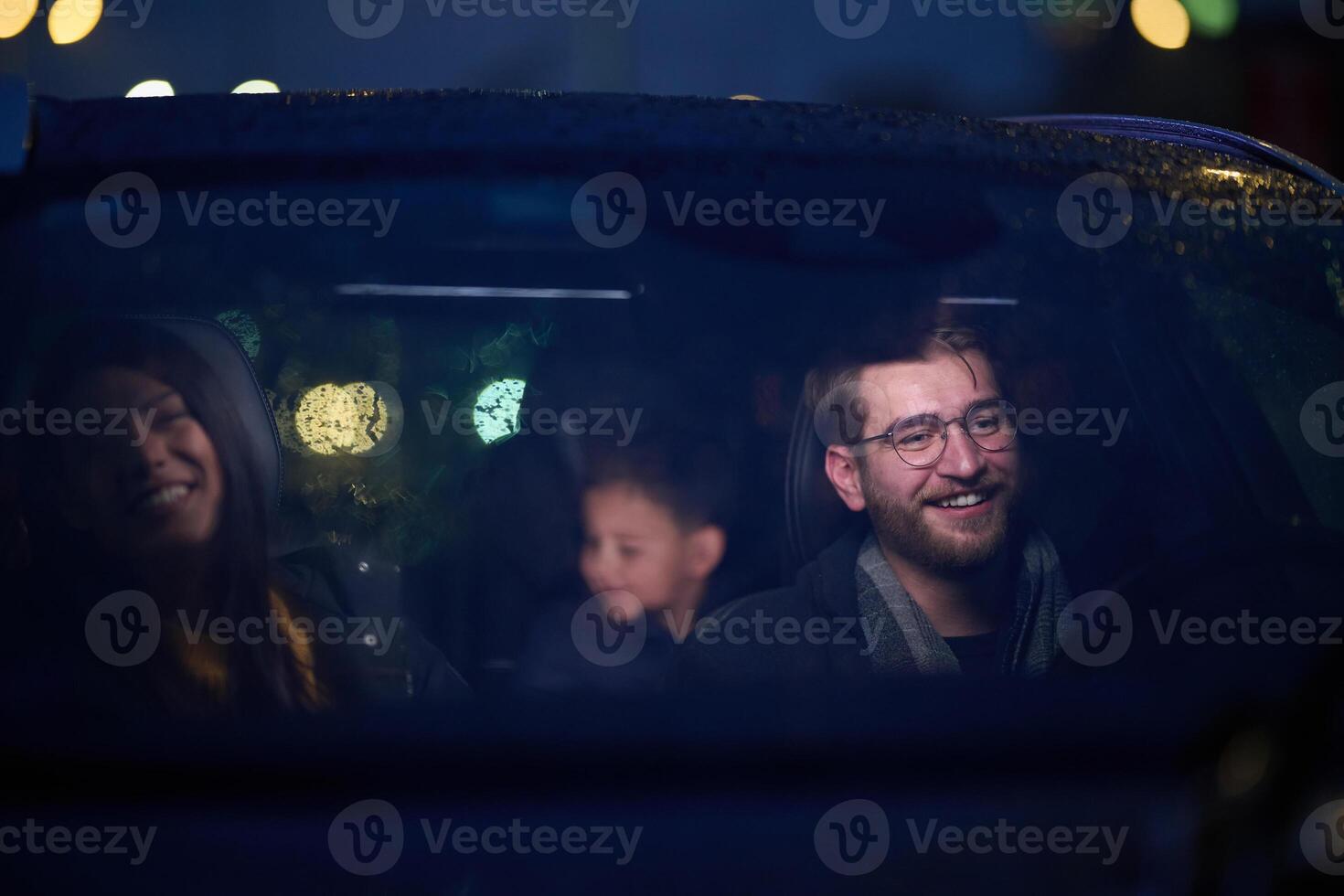 In the nighttime hours, a happy family enjoys playful moments together inside a car as they journey on a nocturnal road trip, illuminated by the glow of headlights and filled with laughter and joy photo