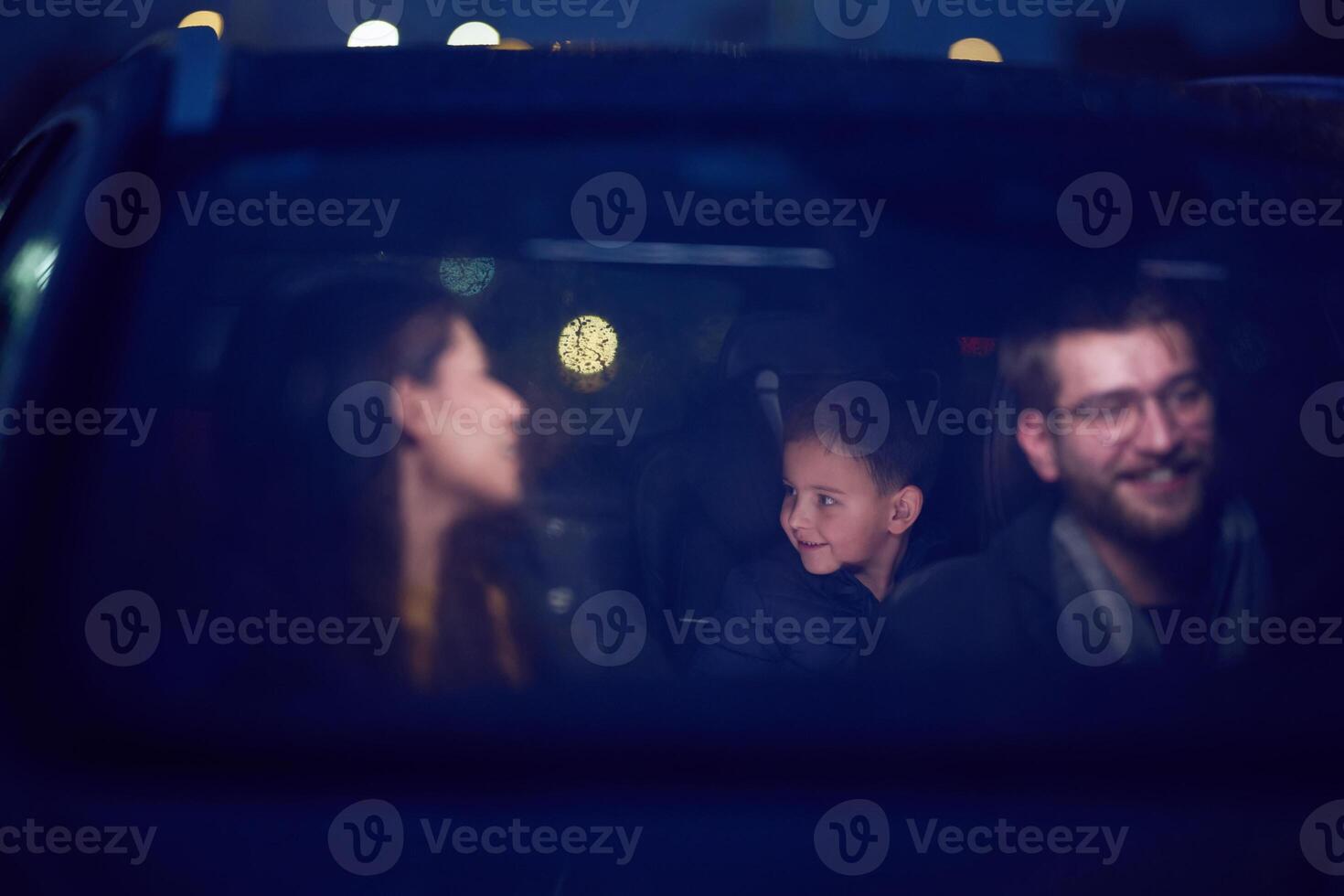 In the nighttime hours, a happy family enjoys playful moments together inside a car as they journey on a nocturnal road trip, illuminated by the glow of headlights and filled with laughter and joy photo