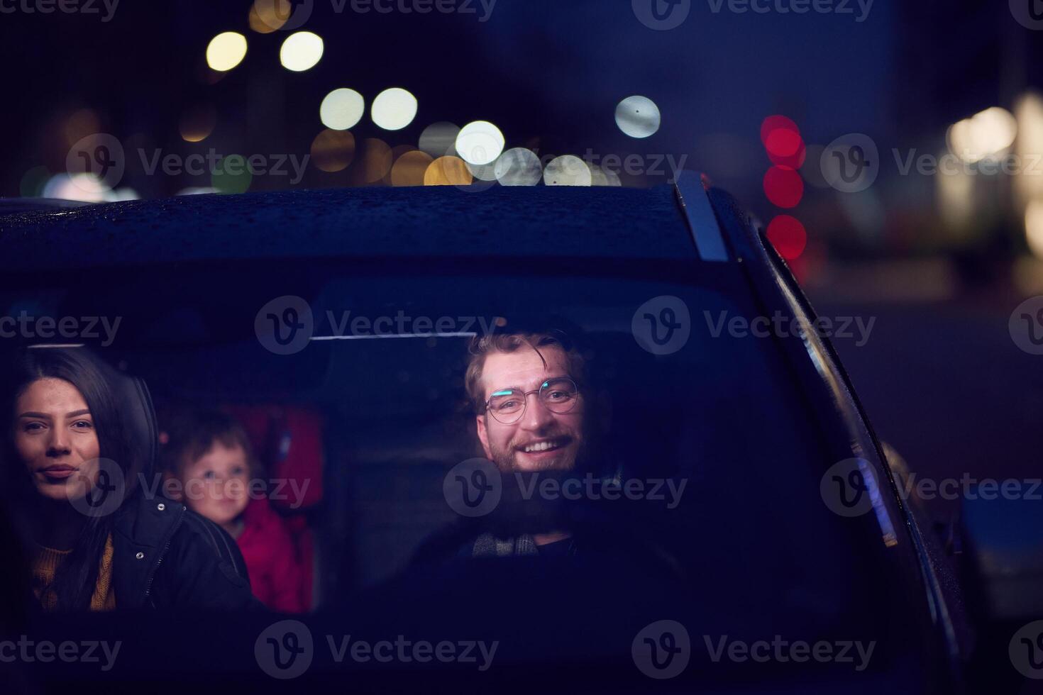 In the nighttime hours, a happy family enjoys playful moments together inside a car as they journey on a nocturnal road trip, illuminated by the glow of headlights and filled with laughter and joy photo