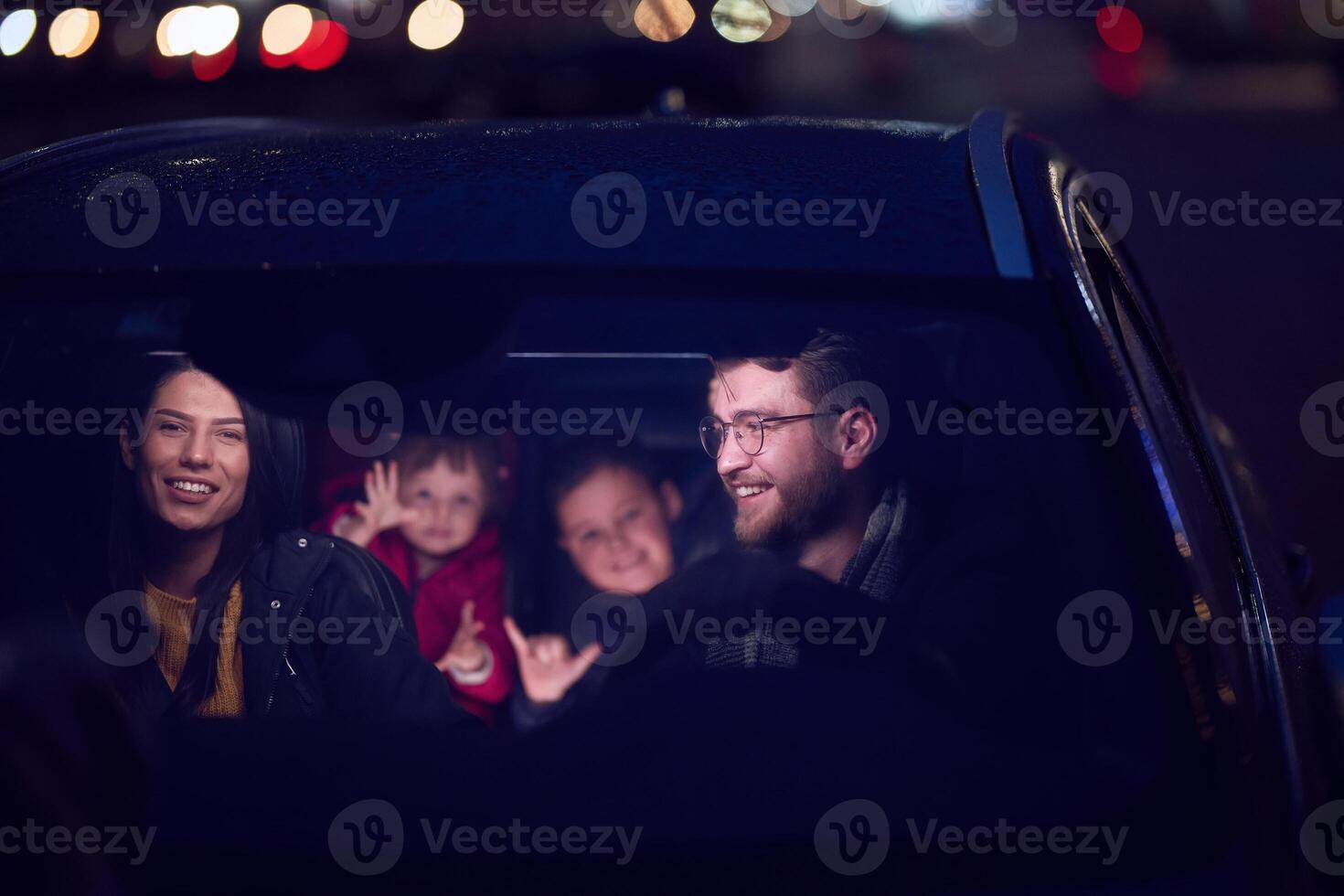 In the nighttime hours, a happy family enjoys playful moments together inside a car as they journey on a nocturnal road trip, illuminated by the glow of headlights and filled with laughter and joy photo