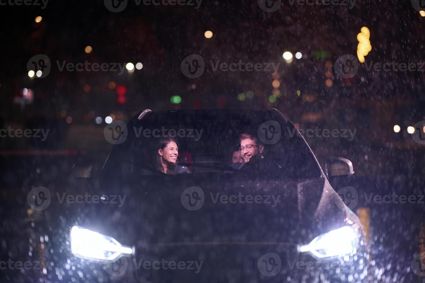 In the midst of a nighttime journey, a happy family enjoys playful moments inside a car as they travel through rainy weather, illuminated by the glow of headlights, laughter, and bonding photo