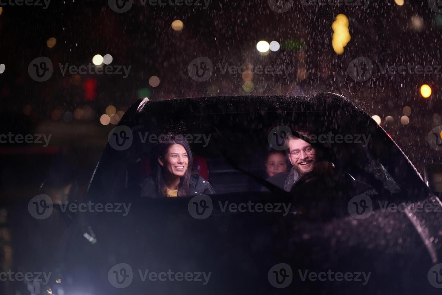 In the midst of a nighttime journey, a happy family enjoys playful moments inside a car as they travel through rainy weather, illuminated by the glow of headlights, laughter, and bonding photo