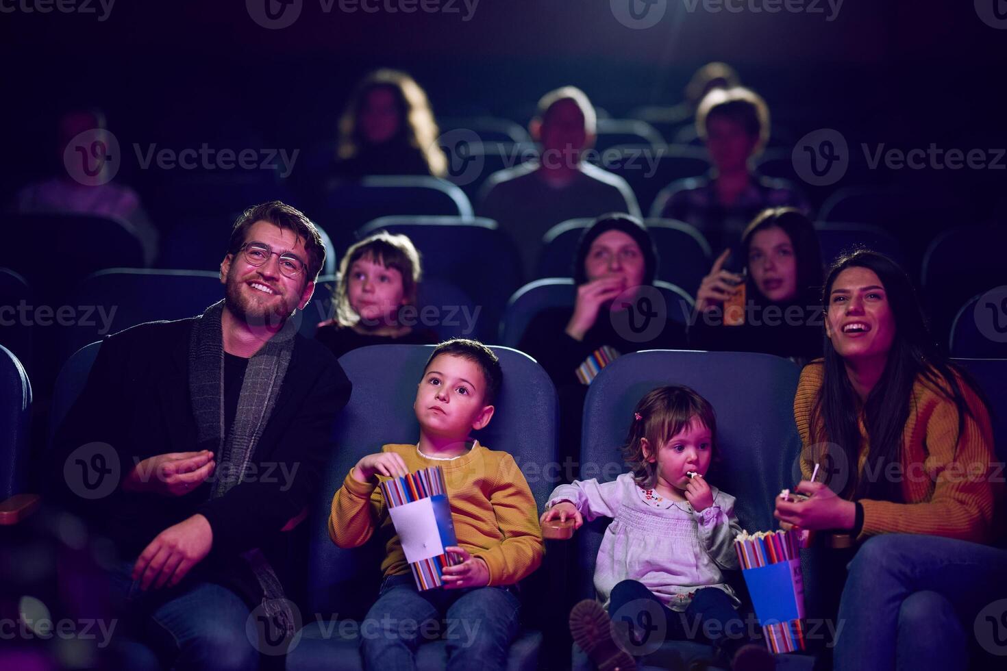 A modern family enjoys quality time together at the cinema, indulging in popcorn while watching a movie with their children photo