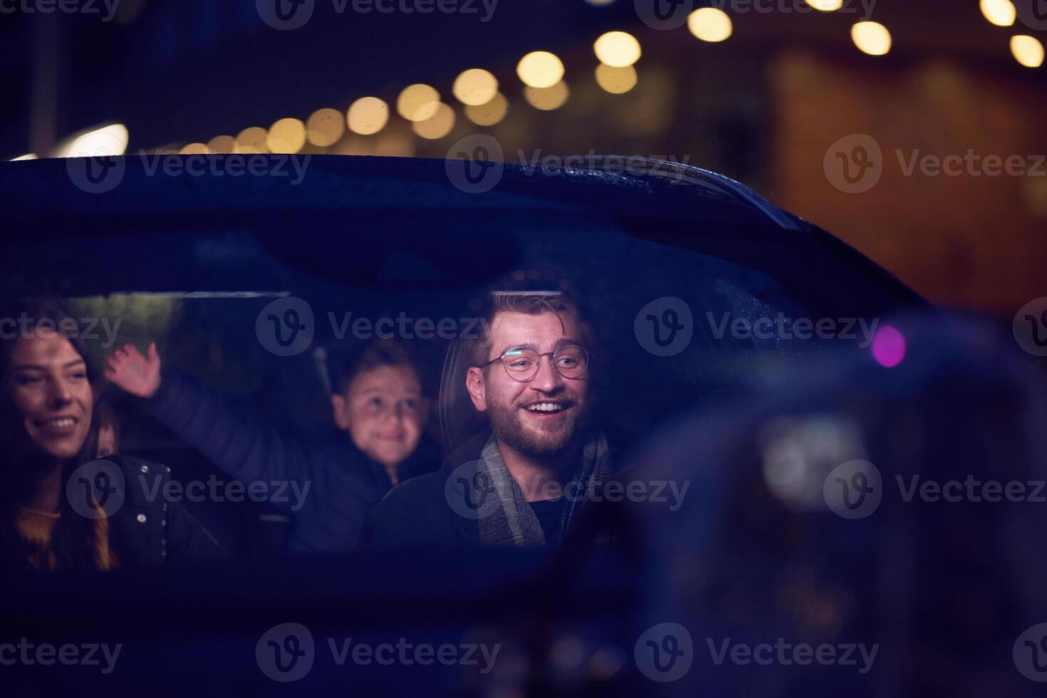 In the nighttime hours, a happy family enjoys playful moments together inside a car as they journey on a nocturnal road trip, illuminated by the glow of headlights and filled with laughter and joy photo