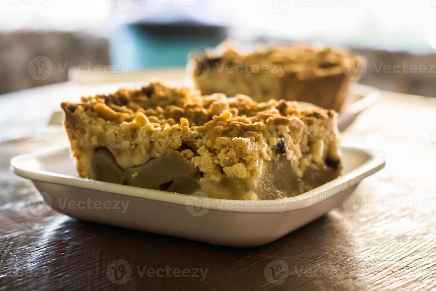 Piece of apple crumble cake on a plastic tray in close-up another one in the background photo