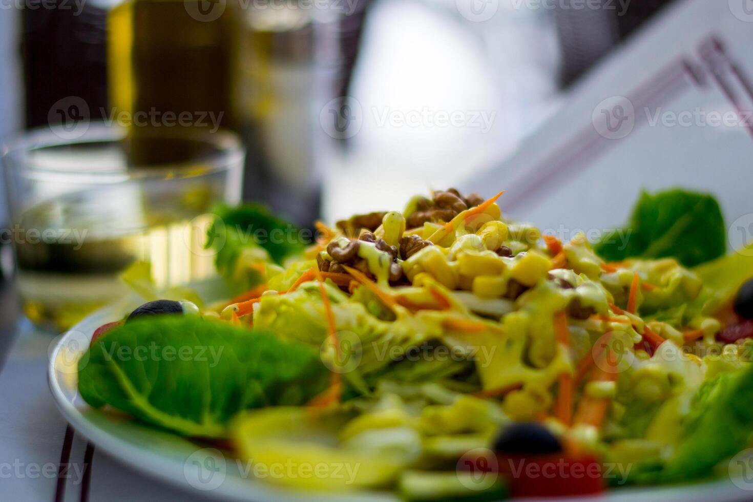 Vegetarian plate with vegetables, mais, salad and nuts, glass of white wine in the background photo