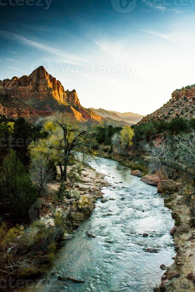View of the Watchman in Zion National Park, Utah with Virgin River flowing to the mountain range during sunset, coloring the rocks orange photo