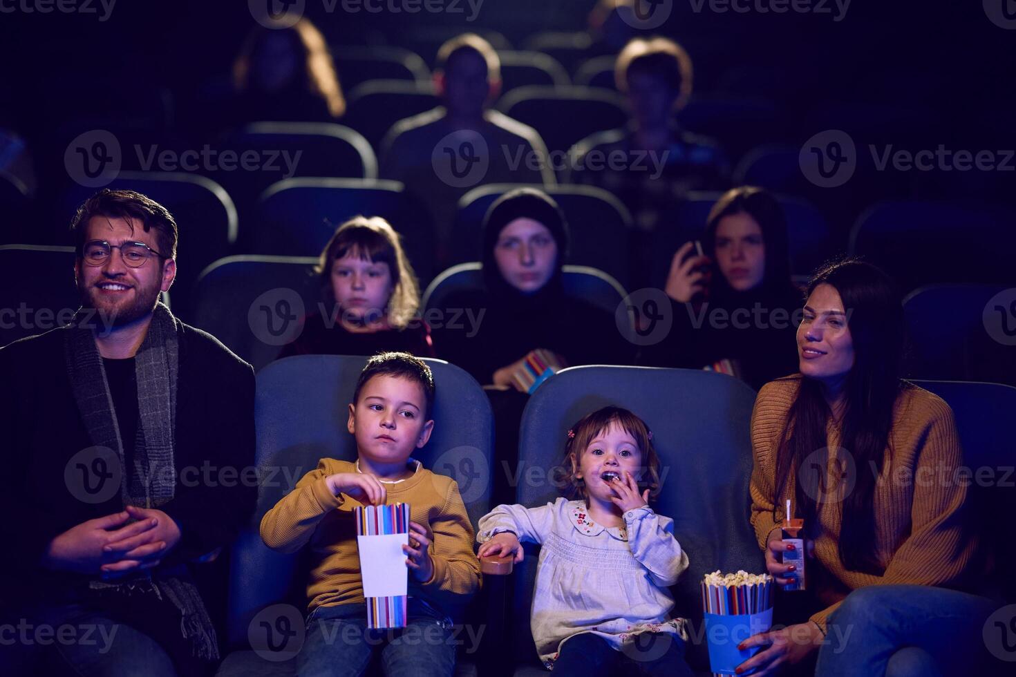 A modern family enjoys quality time together at the cinema, indulging in popcorn while watching a movie with their children photo