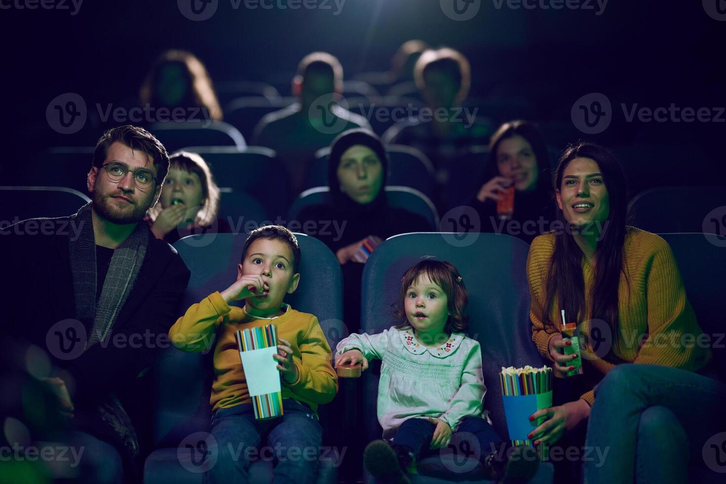 A modern family enjoys quality time together at the cinema, indulging in popcorn while watching a movie with their children photo