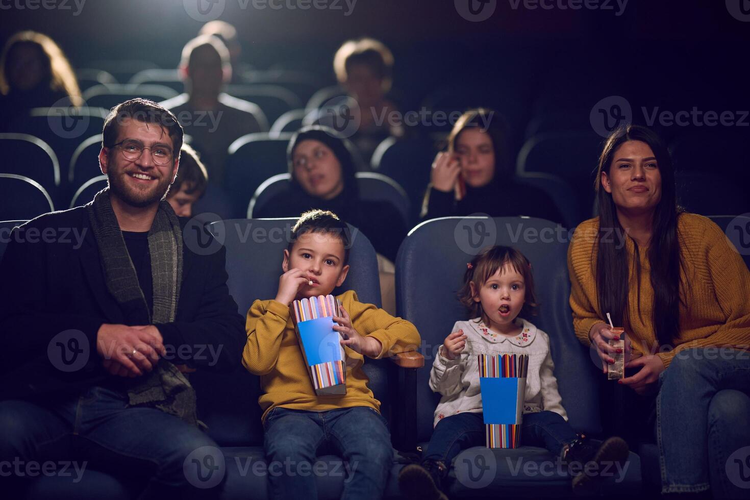 A modern family enjoys quality time together at the cinema, indulging in popcorn while watching a movie with their children photo