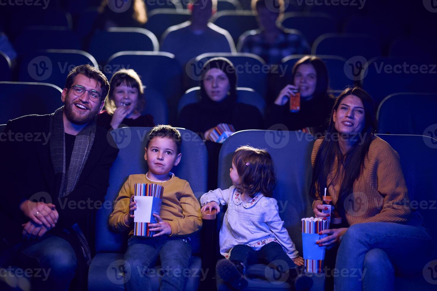 A modern family enjoys quality time together at the cinema, indulging in popcorn while watching a movie with their children photo