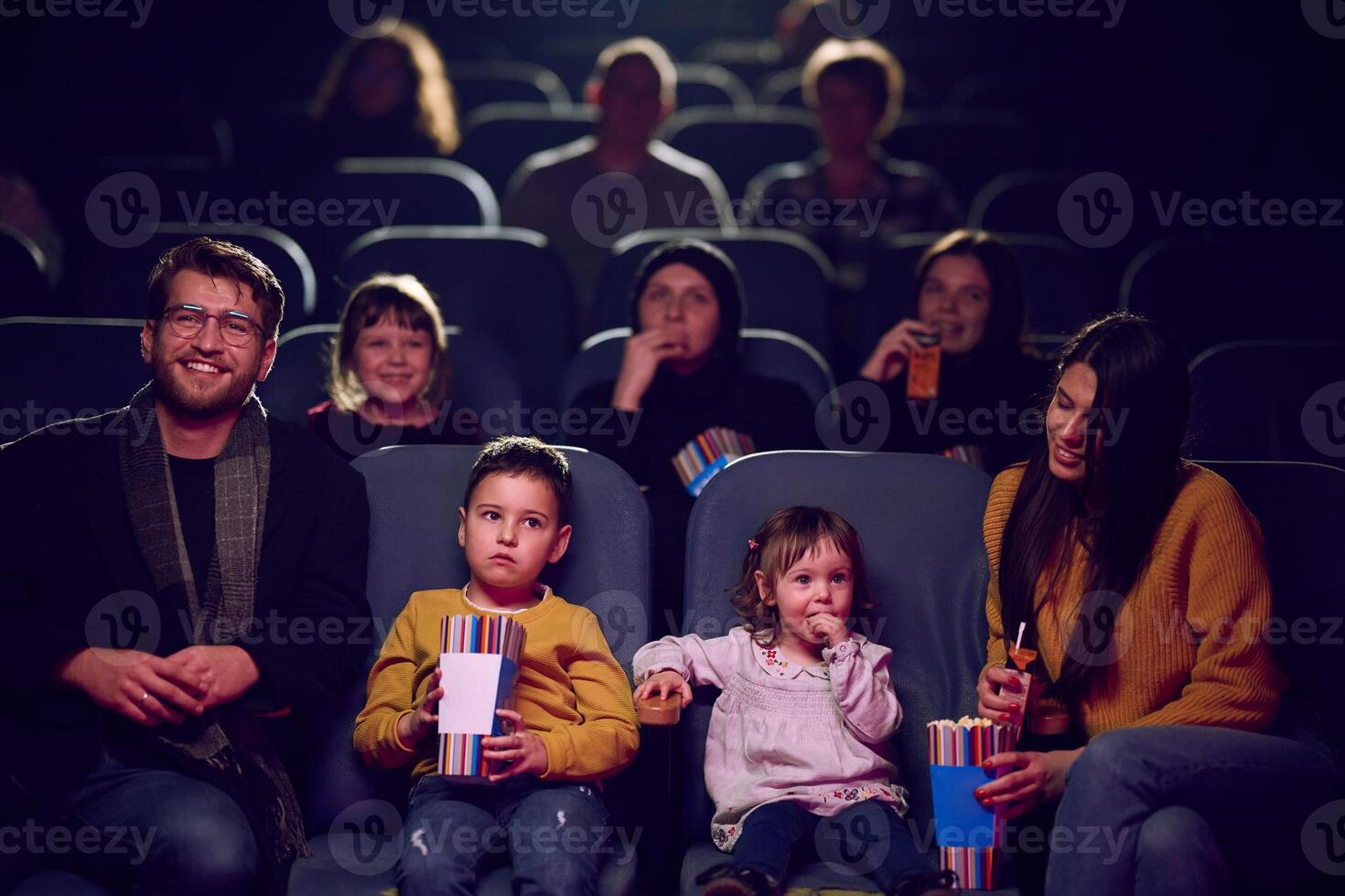 A modern family enjoys quality time together at the cinema, indulging in popcorn while watching a movie with their children photo