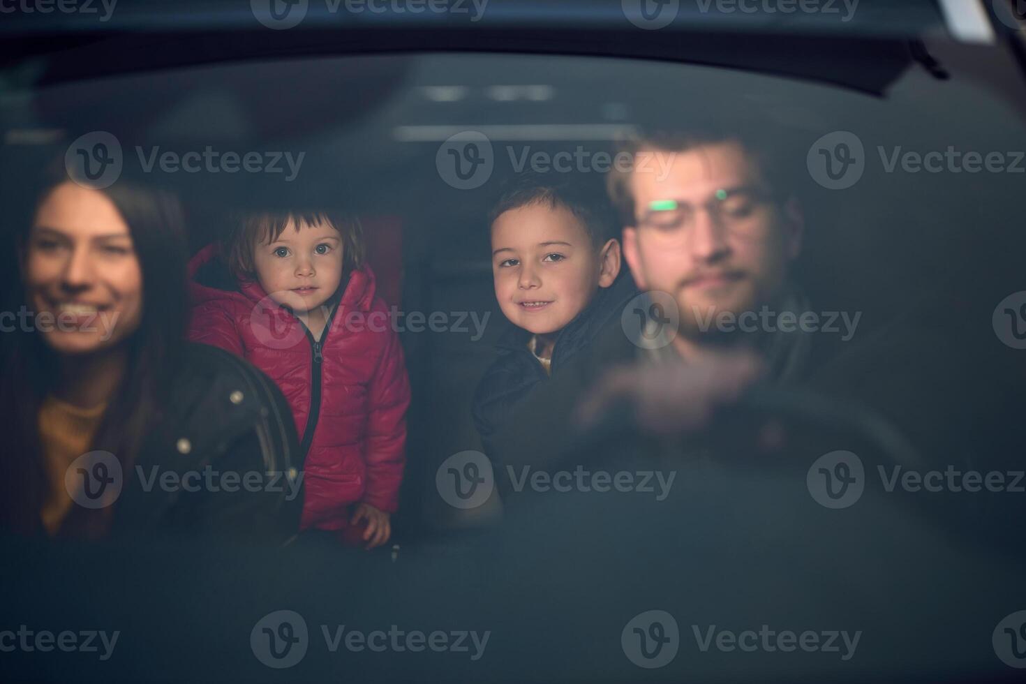 In the nighttime hours, a happy family enjoys playful moments together inside a car as they journey on a nocturnal road trip, illuminated by the glow of headlights and filled with laughter and joy photo