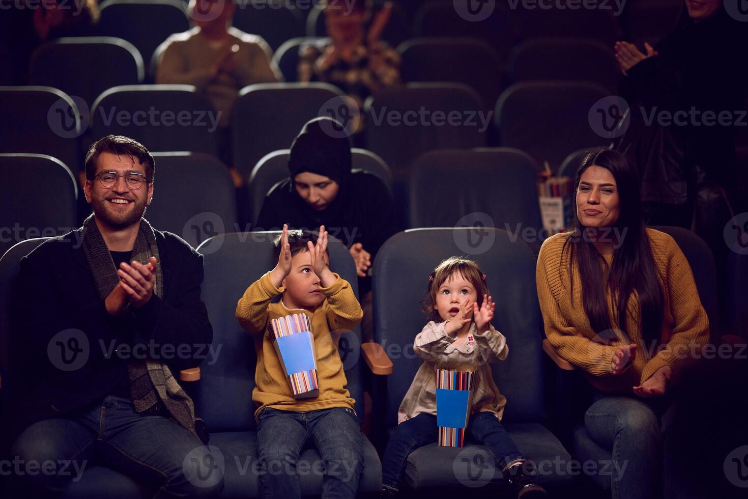 A modern family enjoys quality time together at the cinema, indulging in popcorn while watching a movie with their children photo