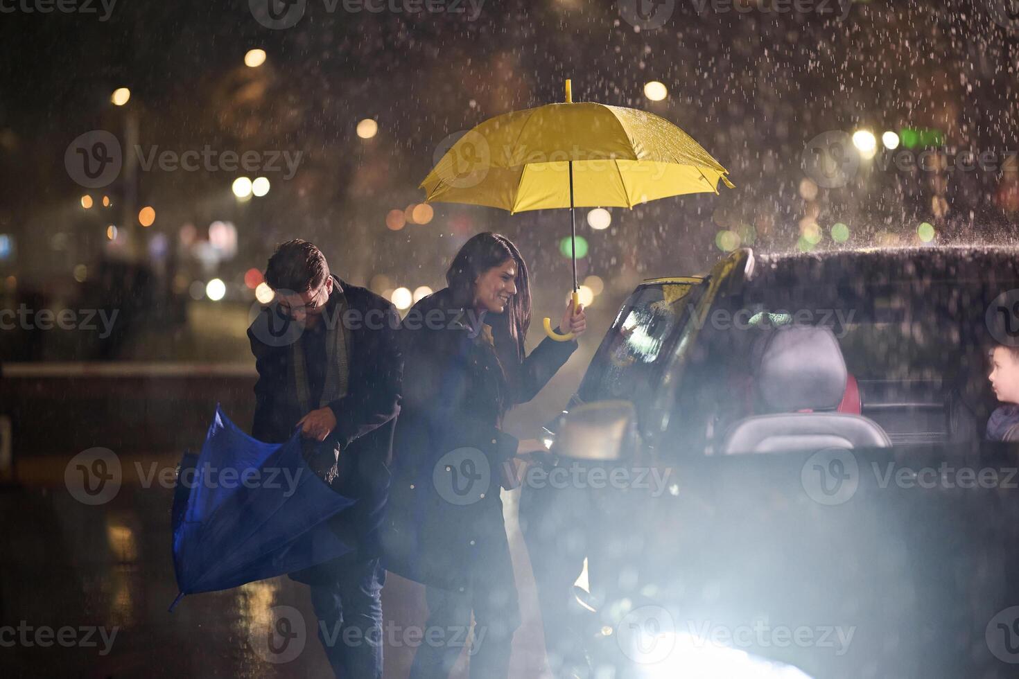 A family man lovingly opens the car for his family in rainy weather, sheltering them with an umbrella photo