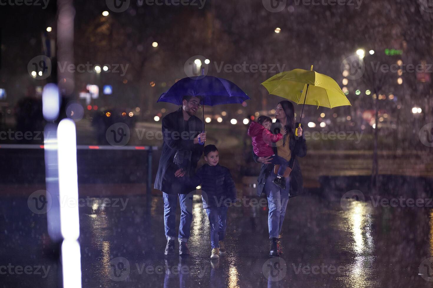 In the midst of a rainy urban night, a happy couple takes their children on a stroll through the city streets, heading towards the cinema for a delightful family movie outing photo