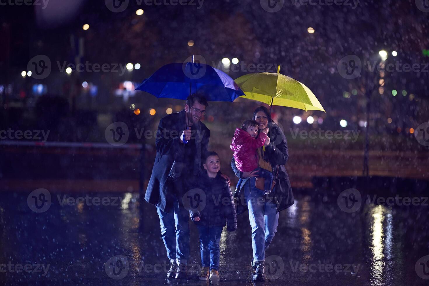 In the midst of a rainy urban night, a happy couple takes their children on a stroll through the city streets, heading towards the cinema for a delightful family movie outing photo