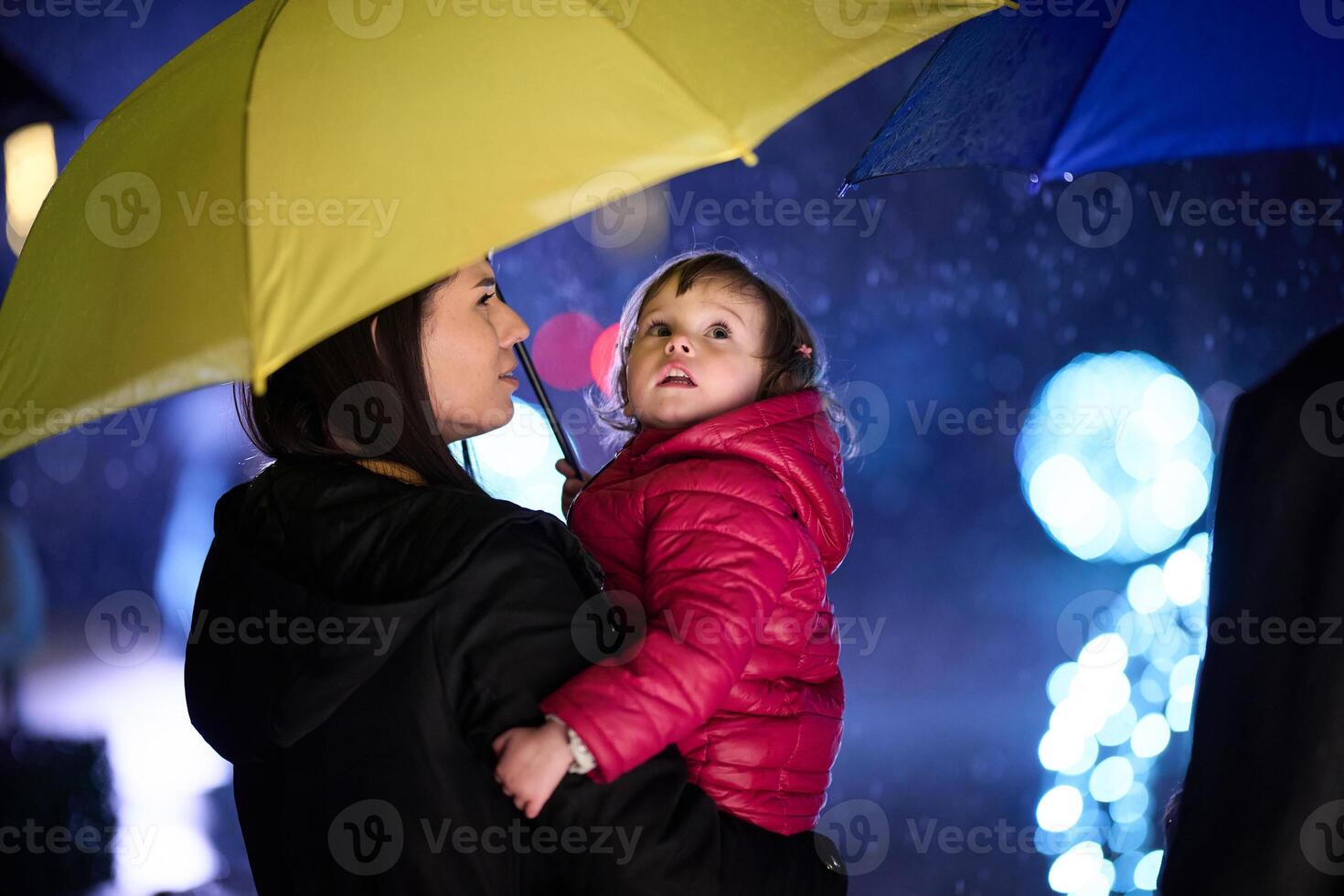 In the midst of a rainy urban night, a happy couple takes their children on a stroll through the city streets, heading towards the cinema for a delightful family movie outing photo