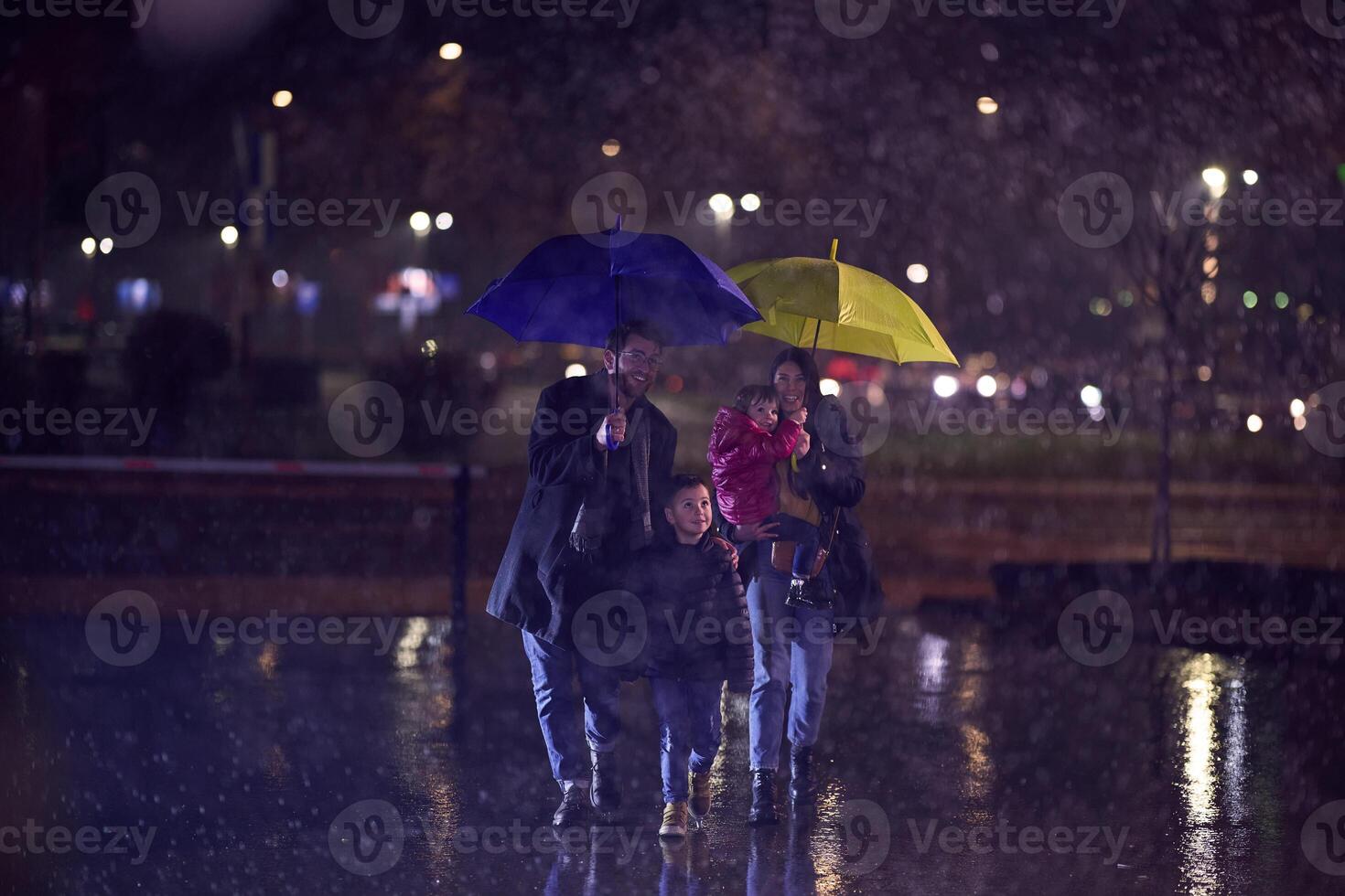 In the midst of a rainy urban night, a happy couple takes their children on a stroll through the city streets, heading towards the cinema for a delightful family movie outing photo