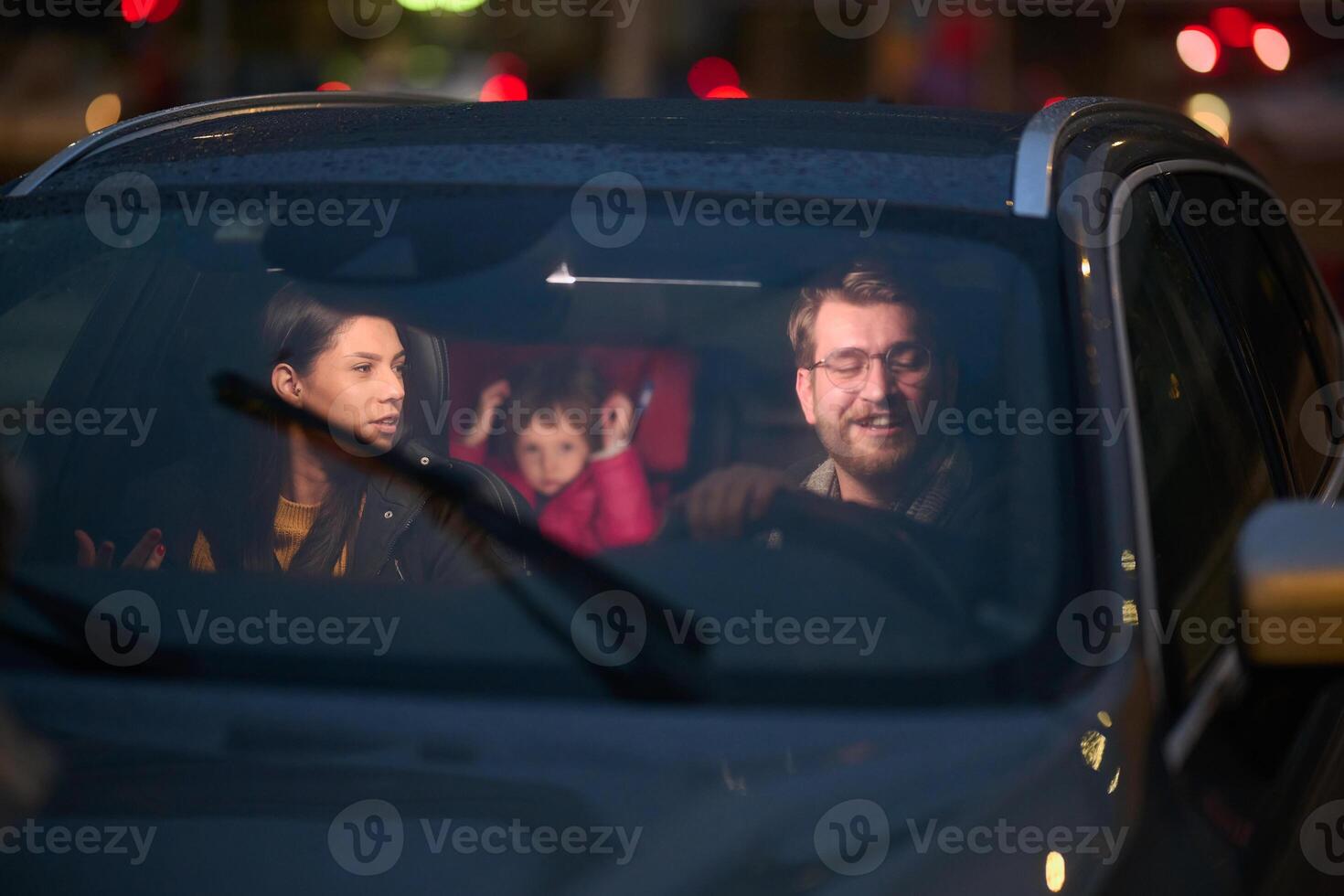 In the nighttime hours, a happy family enjoys playful moments together inside a car as they journey on a nocturnal road trip, illuminated by the glow of headlights and filled with laughter and joy photo