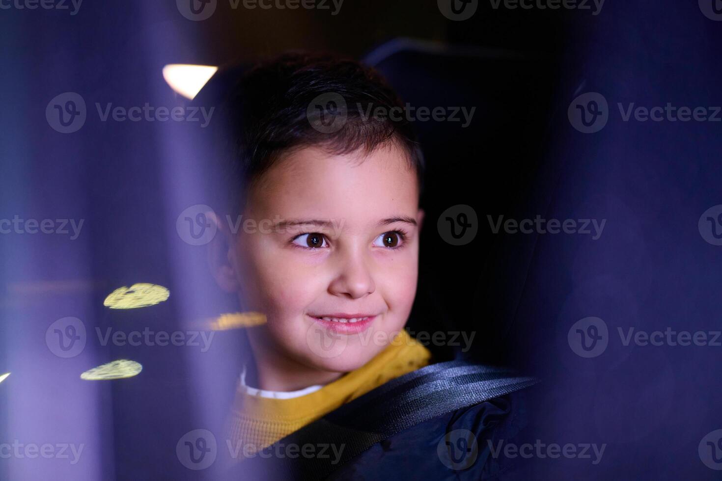 A young boy enjoys a car ride, captured through the window, as he observes the passing scenery. photo