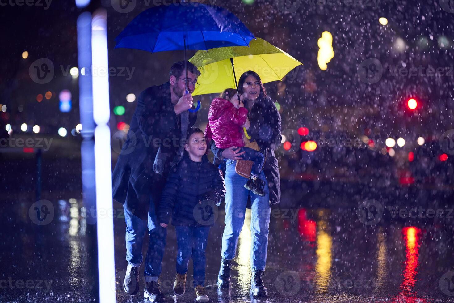 In the midst of a rainy urban night, a happy couple takes their children on a stroll through the city streets, heading towards the cinema for a delightful family movie outing photo