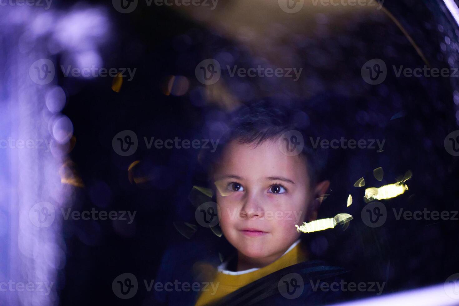 A young boy enjoys a car ride, captured through the window, as he observes the passing scenery. photo