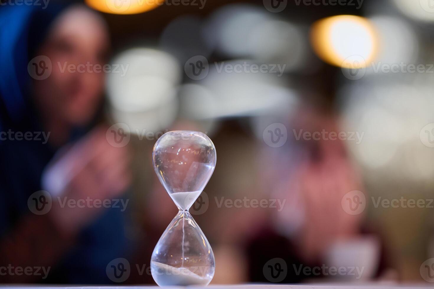 A symbolic hourglass counts down the time to iftar meal, while in the background, an Islamic family devoutly prays, capturing a poignant moment of spiritual connection and anticipation during Ramadan photo