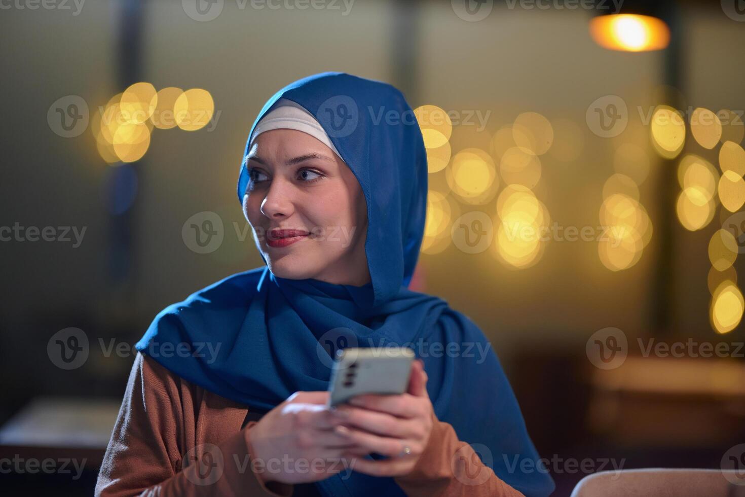 A beautiful European Muslim woman, adorned with a hijab, utilizes her smartphone to swiftly prepare for iftar during the sacred month of Ramadan, embodying the blend of tradition and modernity in her photo