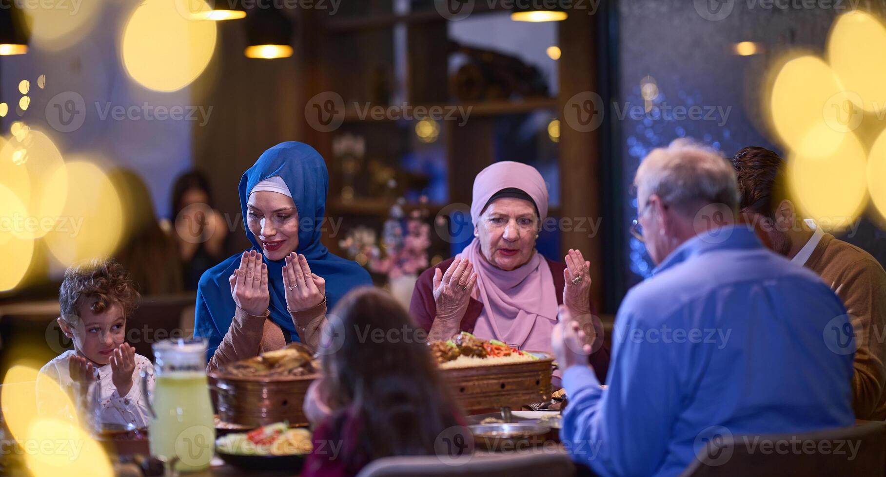 In a modern restaurant setting, a European Islamic family comes together for iftar during Ramadan, engaging in prayer before the meal, uniting tradition and contemporary practices in a celebration of photo