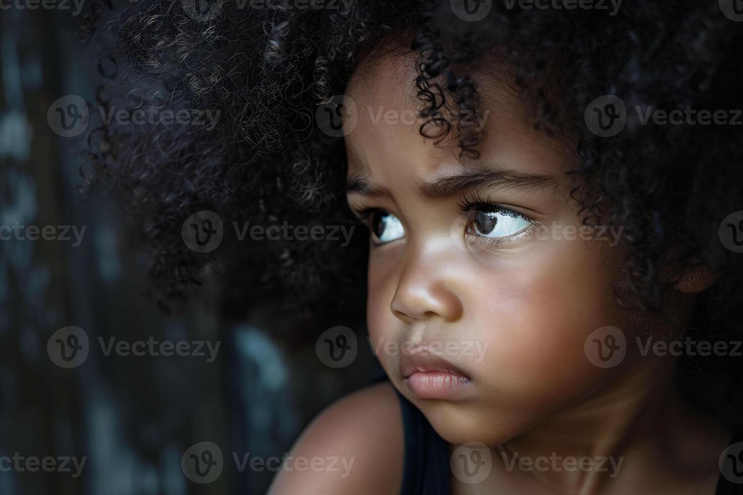 Intense eyes and a cascade of curls frame the pensive face of a young child, absorbed in a moment of quiet reflection, an expression of anger. photo