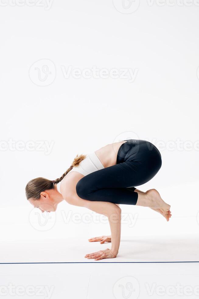 beautiful woman yoga trainer doing bakasana asana on a mat on a white background. photo